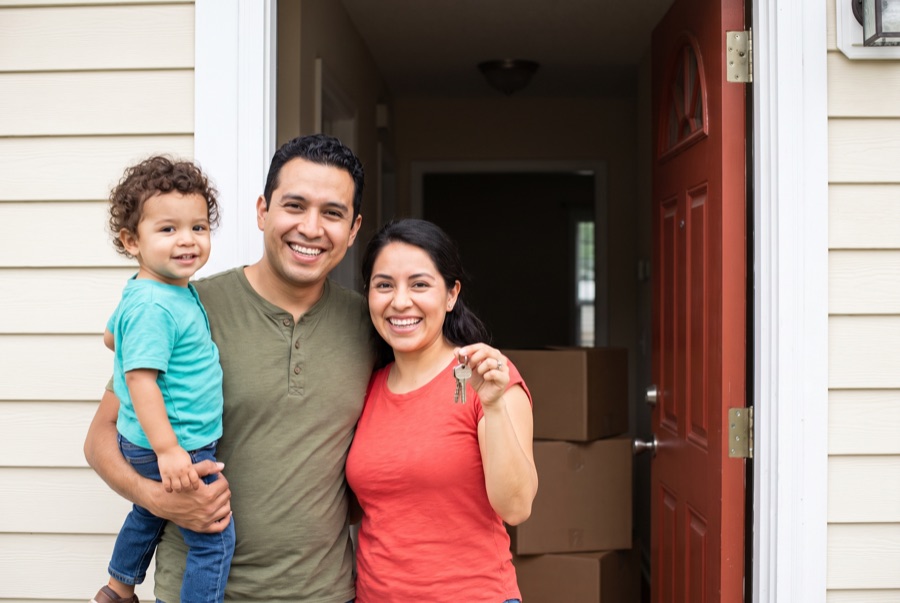 A young couple with their toddler at the door of their first home